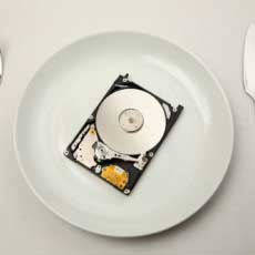 An open hard disk drive on a white plate with a knife and fork... as in consuming technology.