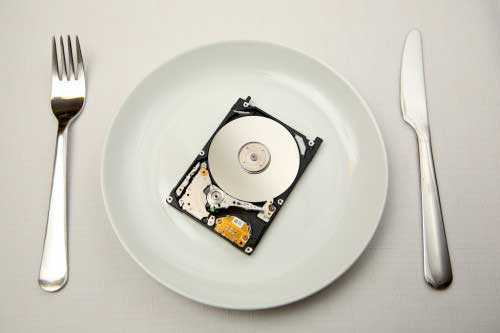 An open hard disk drive on a white plate with a knife and fork... as in consuming technology.