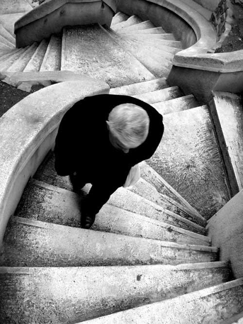 A man is shown from above as he climbs up twisting flights of stairs.