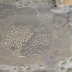 A dusty yin yang symbol made out of dark and light coloured pebbles, set into a concrete floor.