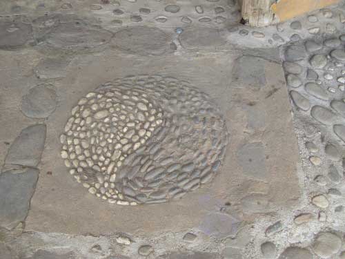 A dusty yin yang symbol made out of dark and light coloured pebbles, set into a concrete floor.