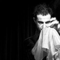 A magician intently focusing on a white handkerchief held in one of his hands.