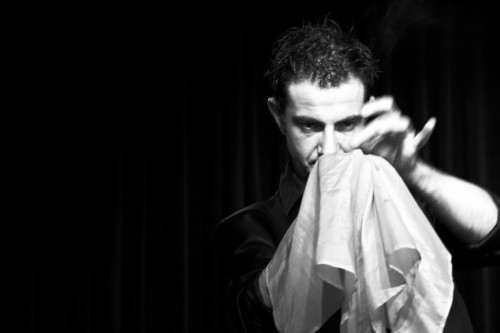 A magician intently focusing on a white handkerchief held in one of his hands.
