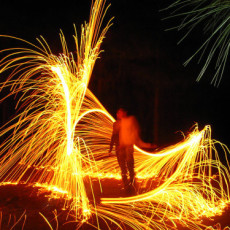 A long exposure in the dark who has danced with a sparkler. It appears that a swirling shower of gold sparks surrounds him.