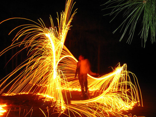 A long exposure in the dark who has danced with a sparkler. It appears that a swirling shower of gold sparks surrounds him.