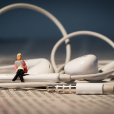 A tiny figure sits on earbuds reading a book, as a depiction of audio books.