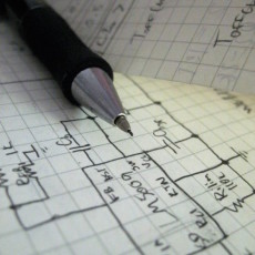 A mechanical pencil rests atop a detailed drawing of a circuit on graph paper.