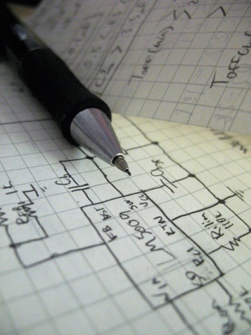 A mechanical pencil rests atop a detailed drawing of a circuit on graph paper.