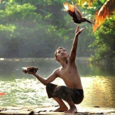 A boy on a raft holds one bird and releases another.