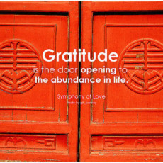 Gratitude inspires abundance. Two wooden red doors with carved symbols, with the words "gratitude is the door opening to the abundance in life.
