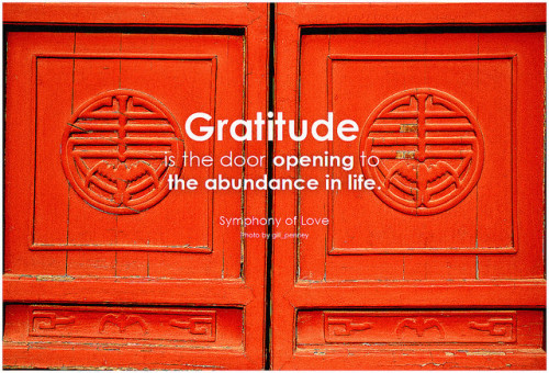 Gratitude inspires abundance. Two wooden red doors with carved symbols, with the words "gratitude is the door opening to the abundance in life.