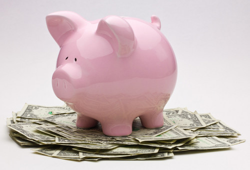 Consider having Less Stuff More Abundance. Pink piggy bank on top of a pile of US one dollar bills