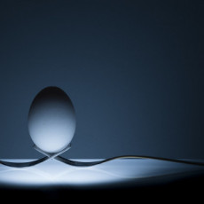 Life lessons are often about balance. An egg perfectly balances on two interlaced forks, sitting on an underlit table.